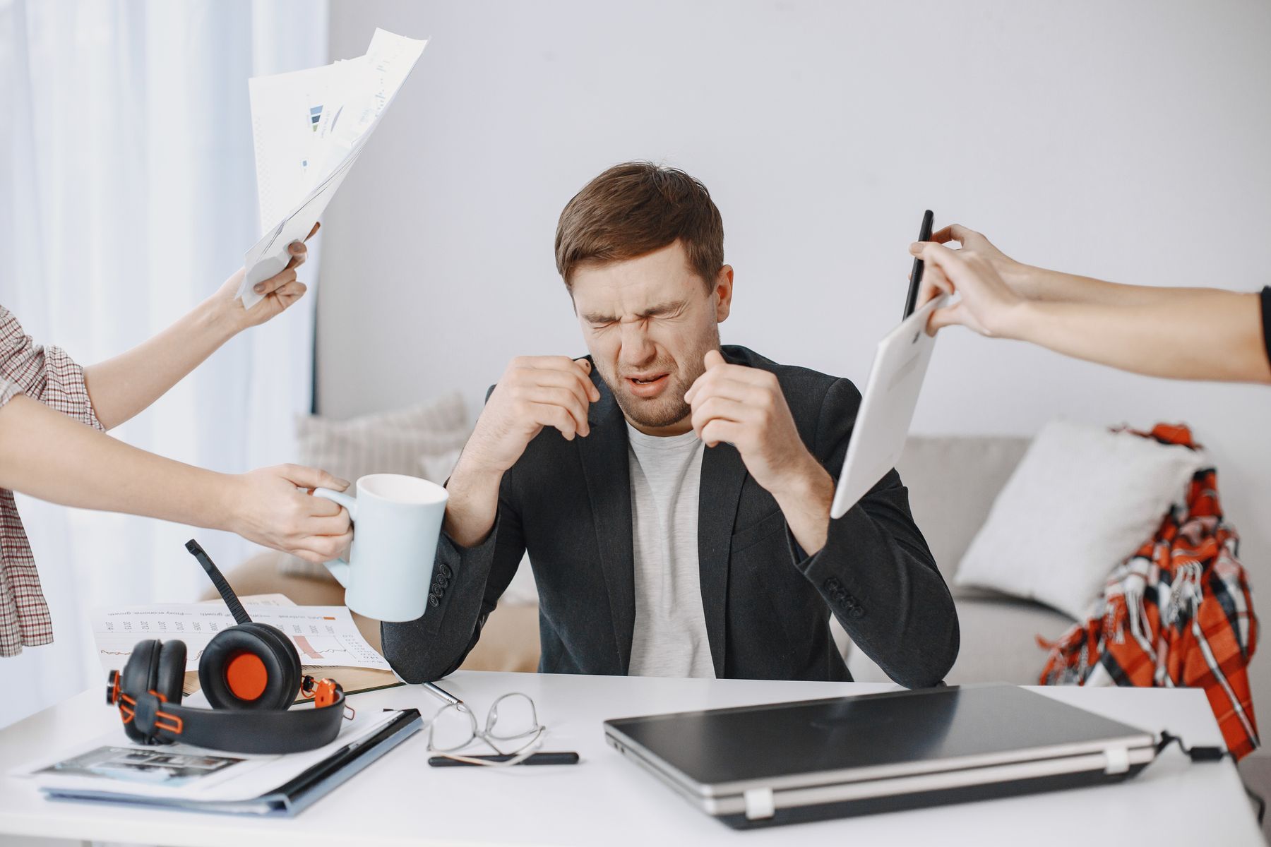 Man at a busy desk overwhelmed by many hands passing him tasks