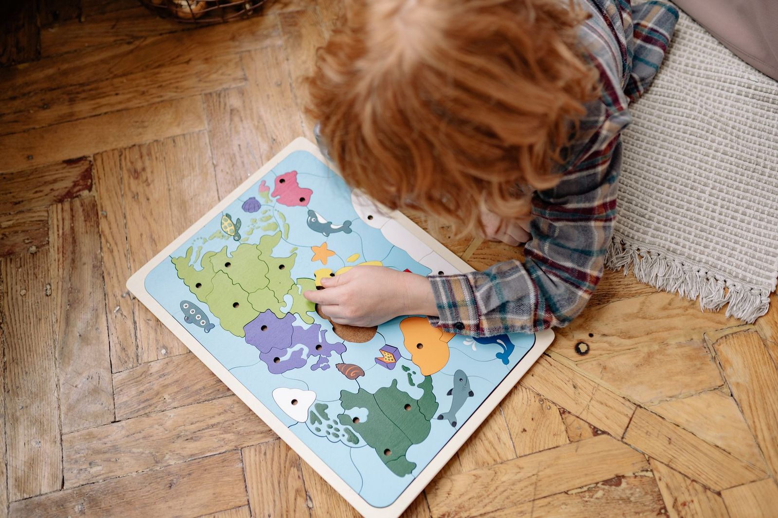 Child working on a world-map jigsaw puzzle on a wooden floor