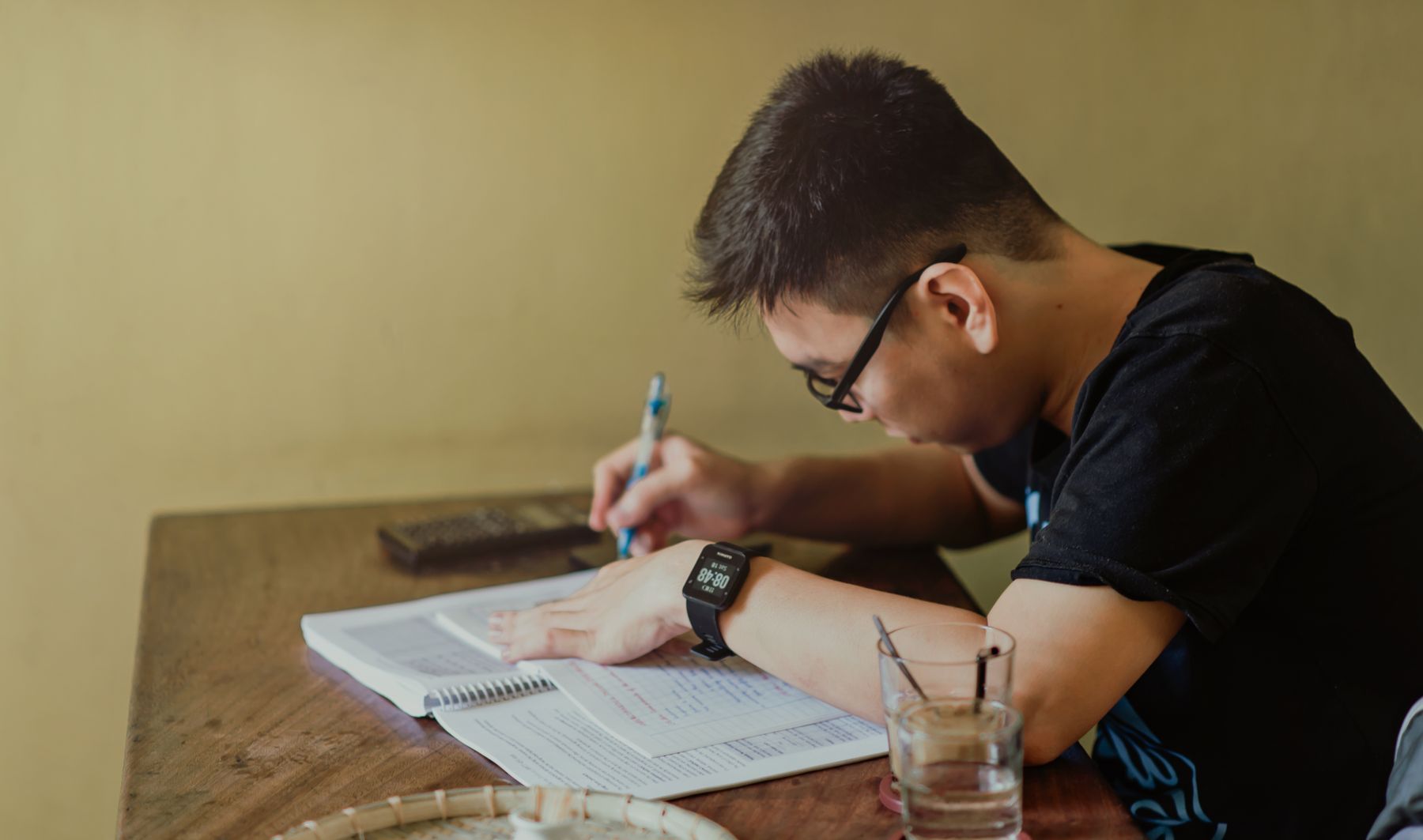 Young man in a black shirt writing at a desk