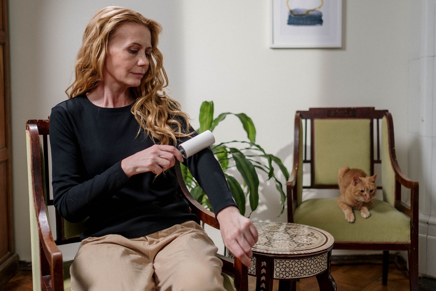 Woman in an armchair using a lint remover on her sweater